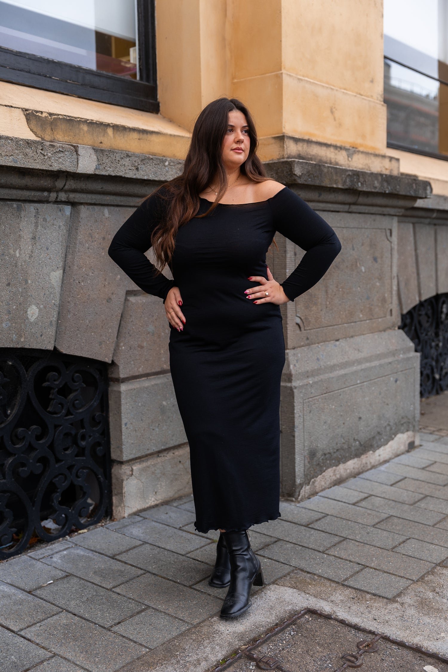 Woman in black dress standing on a sidewalk with a building in the background