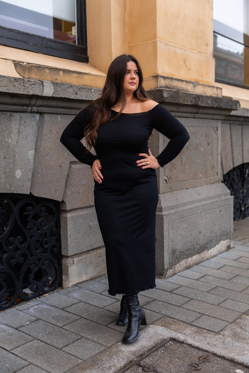 Woman in black dress standing on a sidewalk with a building in the background